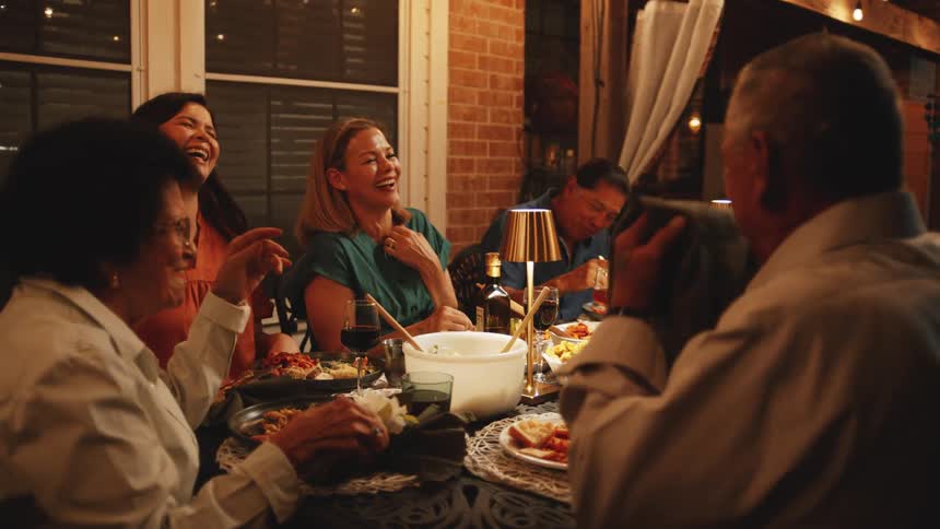 A group of people laughing and conversing at an indoor family dinner during nighttime