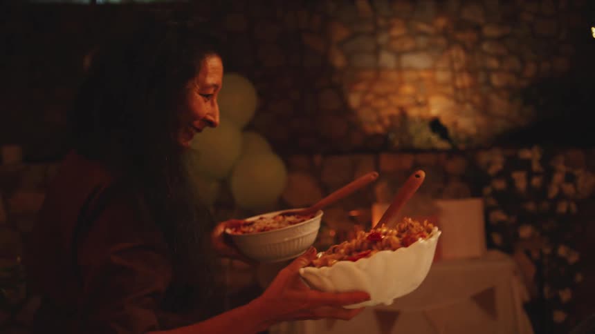 Person places a salad on a set table with glasses candles and warm lighting