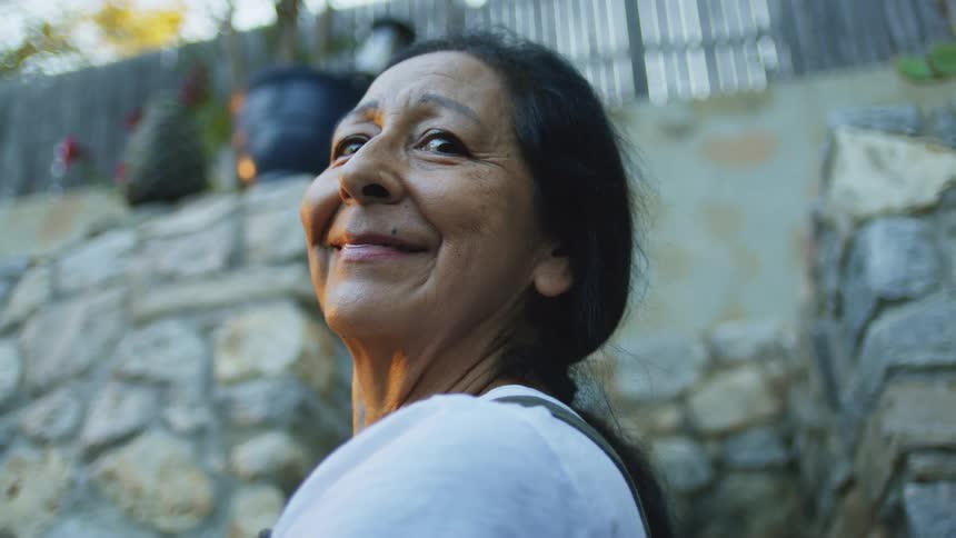 The woman is smiling in front of the stone wall