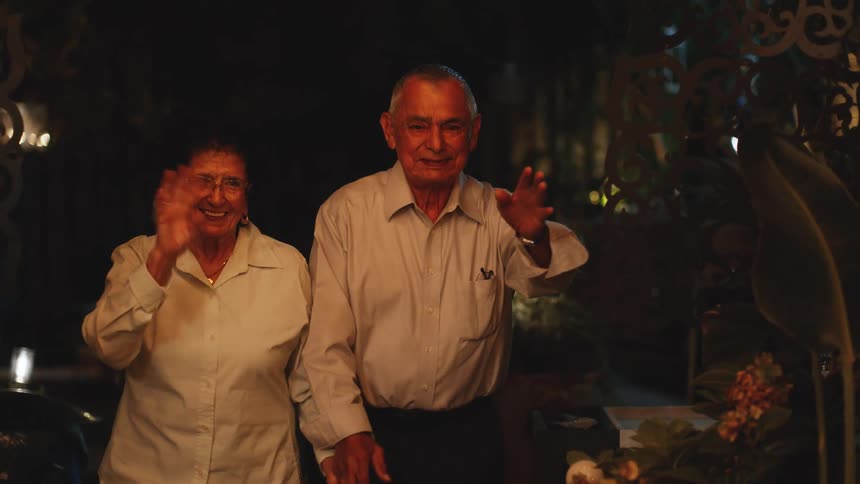 Elderly couple smiling and waving in a warmly lit evening setting