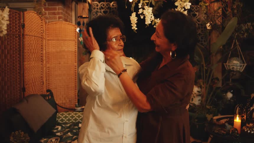 Women smile and embrace in a setting decorated with lights and flowers