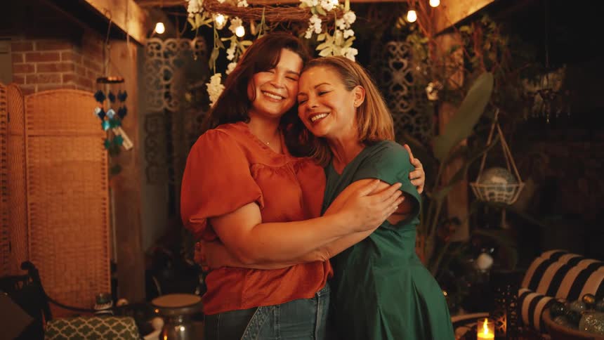 Two women are inside and hug each other laughing and smiling