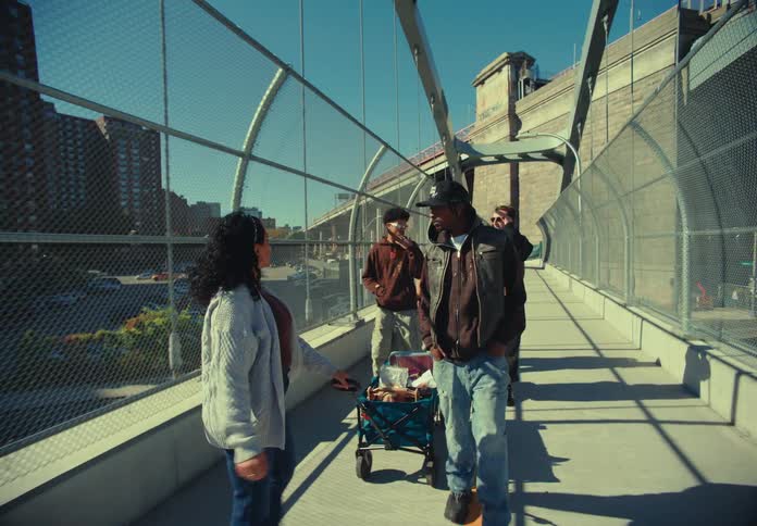 Group of friends crosses a sunny footbridge pulling a cart with items