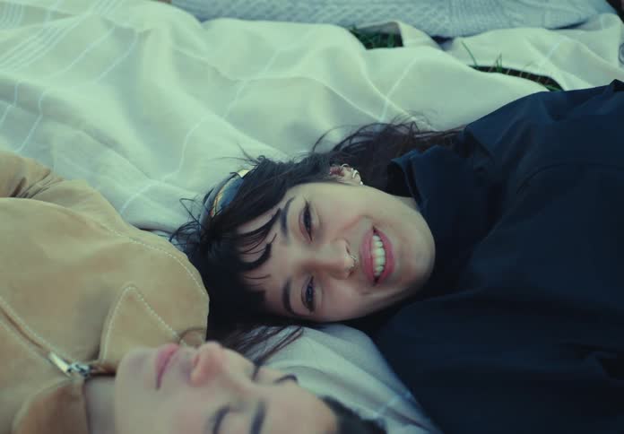 Two women lying on a blanket outdoors share calm gentle looks
