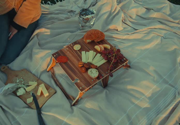 Hand reaches for snacks on a board with cheese fruits and bread on a blanket