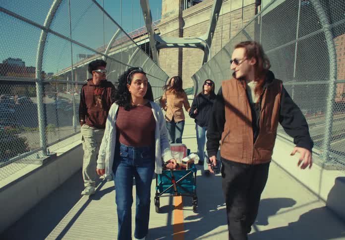 Group of friends walks across a fenced footbridge on a sunny day