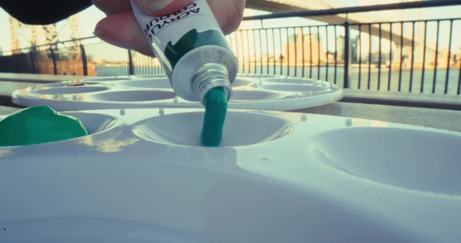 A hand squeezes green paint onto a palette outdoors
