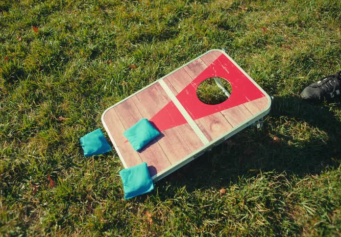 Person arranges blue bean bags on a game board placed on the grass