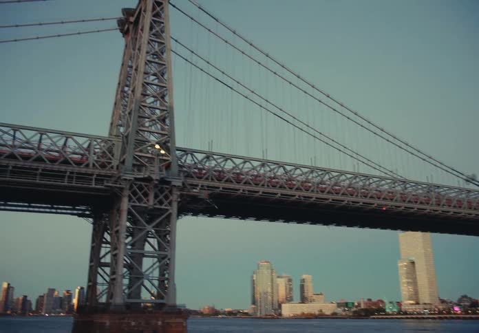 Suspension bridge spans the river with lit buildings in the background