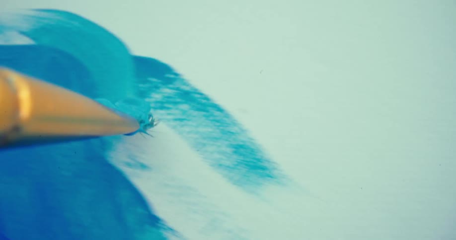 A closeup shot of a paintbrush shows it first swirling blue paint on a palette then spreading a thick layer of blue paint across a white canvas creating visible brushstrokes