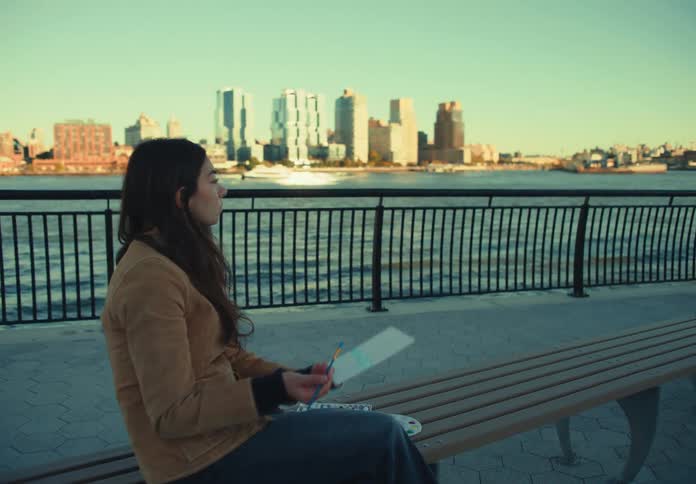 Woman painting on a bench near a bridge over the river