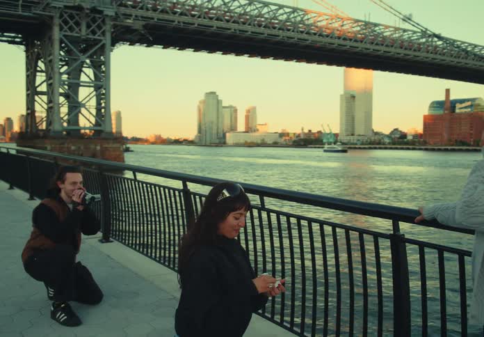 A lesbian couple shares a proposal on a waterfront promenade with a bridge and city skyline