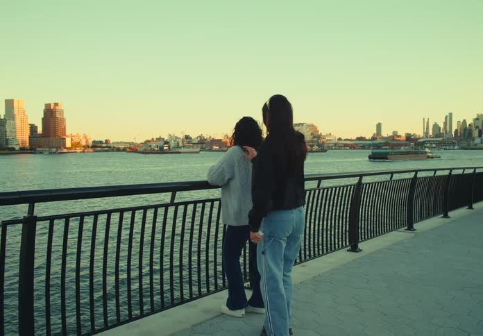 A lesbian couple celebrates a proposal by the waterfront with a city skyline