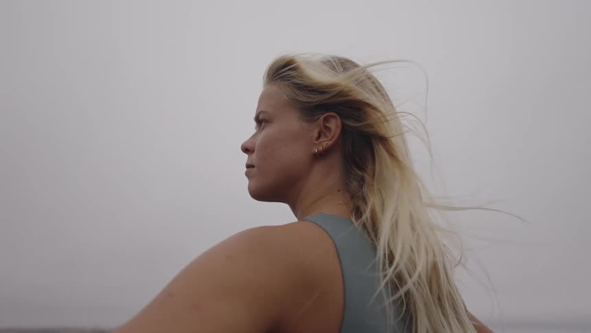 A young blonde woman outdoors standing with her hands on her hips observing the landscape