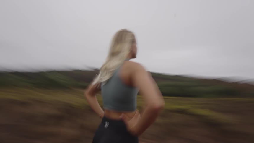 The video is a quick closeup shot of a woman with blonde hair running intensely towards the camera suggesting an energetic workout her face shows concentration as she runs outside against a blurry bright background