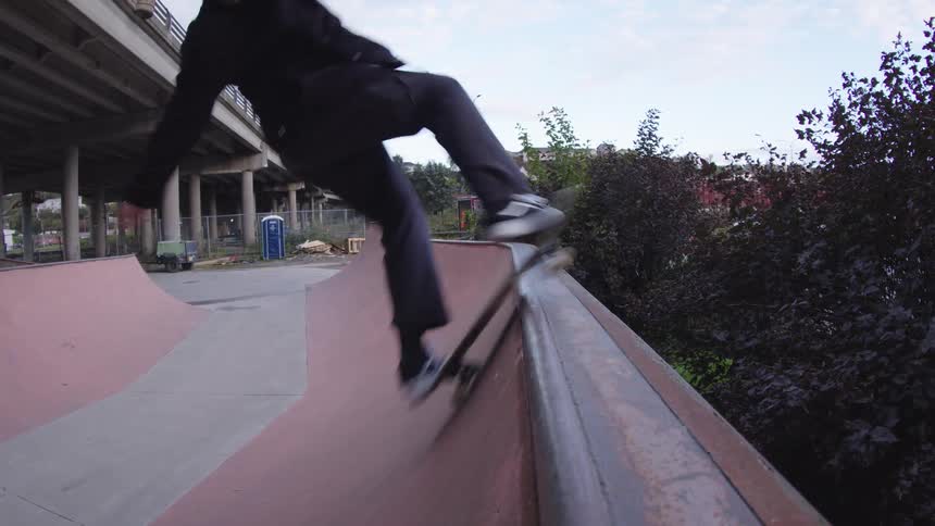 A young man performs a stunt while riding a skateboard on a ramp in a skatepark at midday