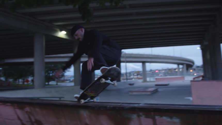 Skateboarder performs a trick on a ramp under an overpass at dusk