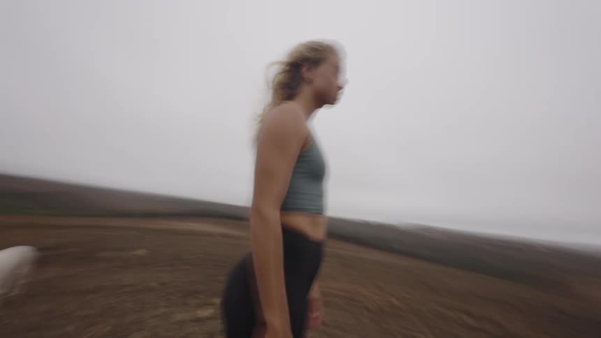 Woman in athletic wear stands in an open field under a cloudy sky