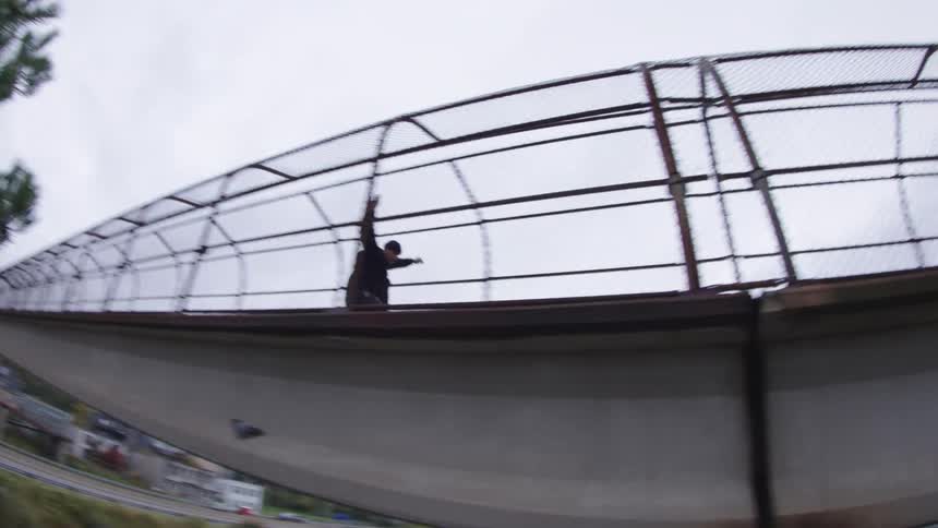 Person skateboards across a metal overpass with side fences