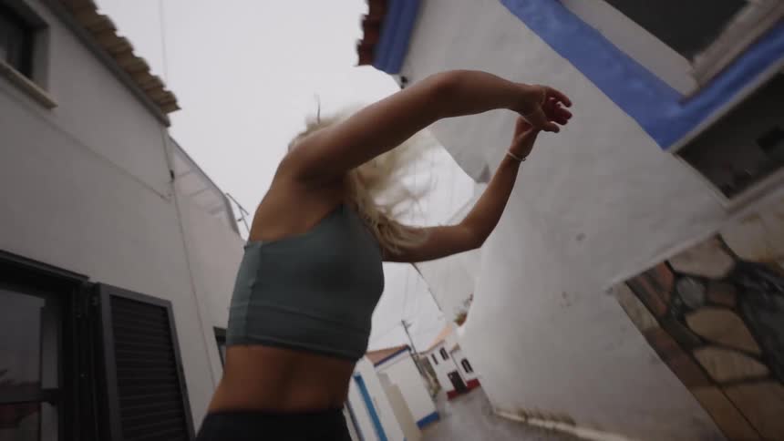 Woman stretches her arms in a narrow street surrounded by white walls