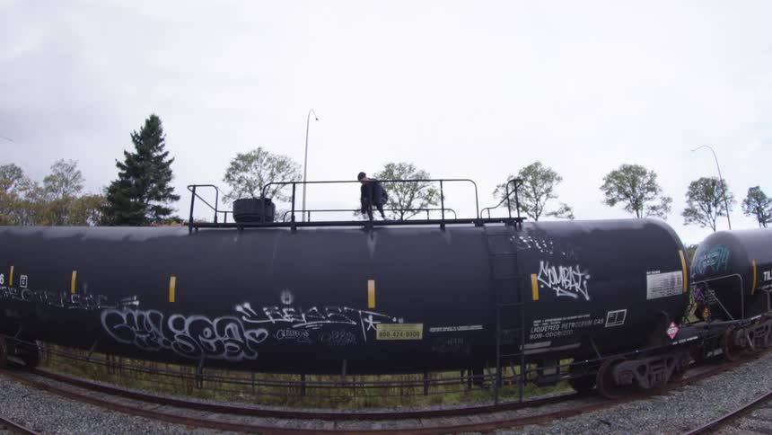 The skateboarder is skating on top of a train tanker