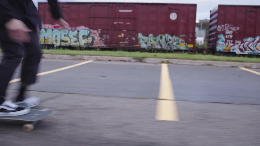 Man wearing dark clothes skateboarding outdoors on a parking space during day time
