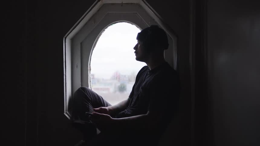 Man sitting on the window sill listens to music on his headphones