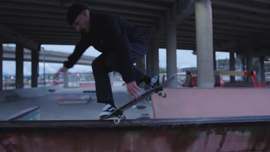 A young man rides a skateboard on a ramp performing a fun stunt in a skateboarding park at midday