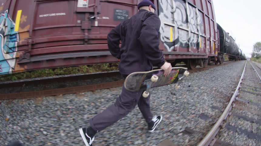 The man drops his skateboard and runs by the tracks