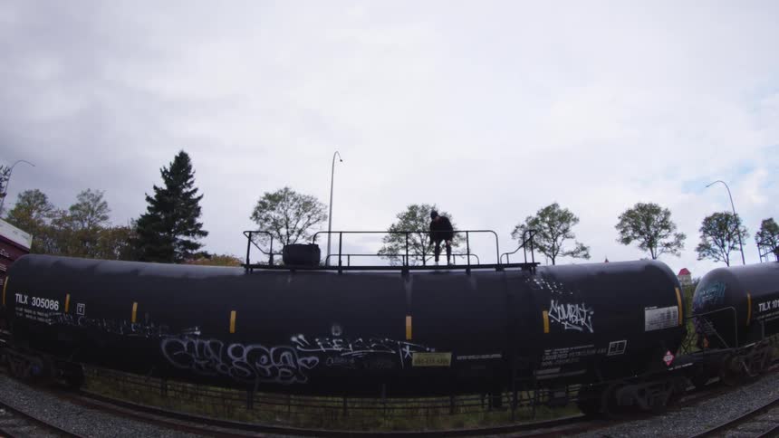 The man skateboards over the large railroad tanker
