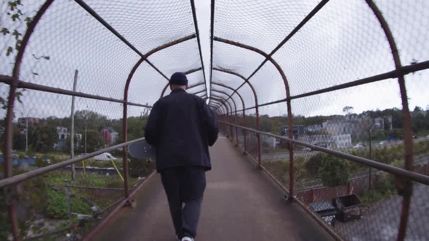 The man walks over the overpass carrying a skateboard