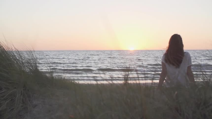 Woman sits by the shore at sunset