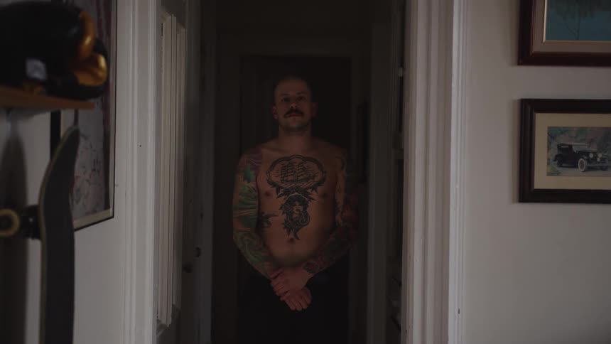 The tattooed man stands in the hallway