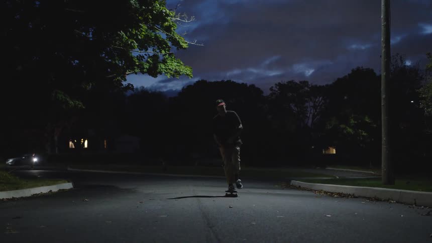 Skateboarder glides down a lit street at night under a partly cloudy sky