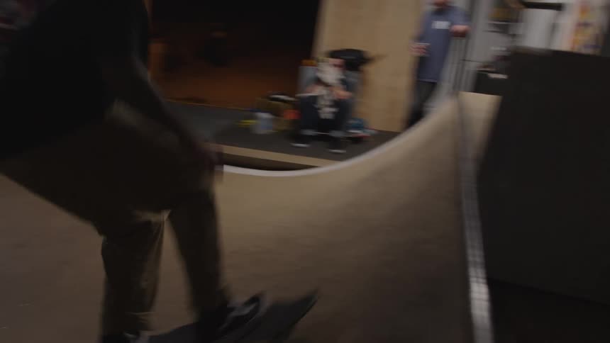 A young male adult skateboarding on an indoor ramp in a garage at night