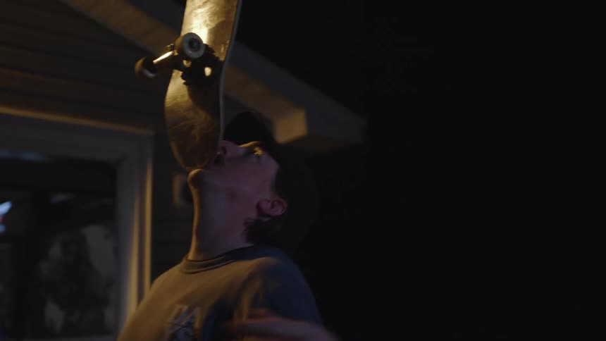 Man balances a skateboard on his face at night
