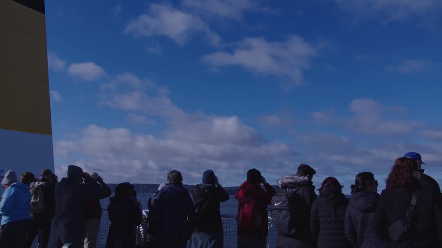 Group of people watches the sea horizon under a blue sky with scattered clouds