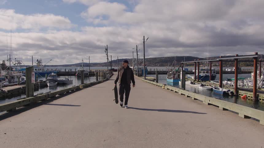 A man walks down a pier holding a skateboard