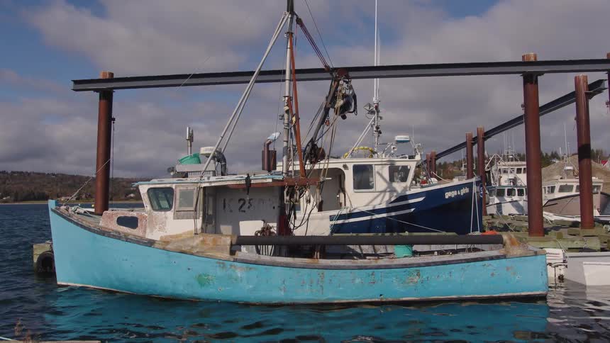 Blue fishing boat docked at a small harbor under a partly cloudy sky
