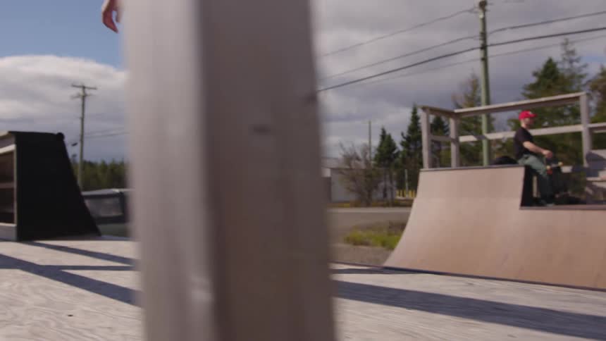 Skateboarder walks toward the ramp holding the skateboard under the afternoon sun