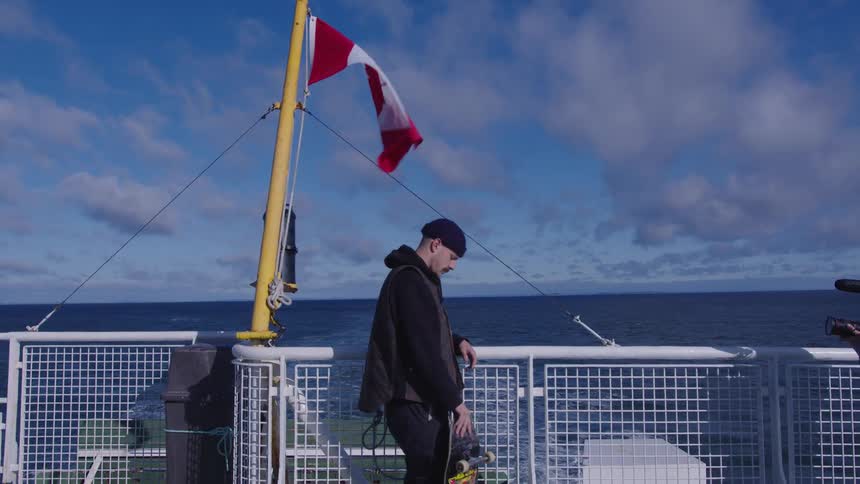 Man looks at the sea while holding a skateboard on the ships deck