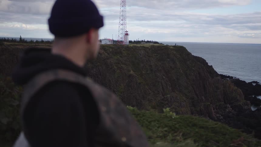 The man is standing and looking at the ocean