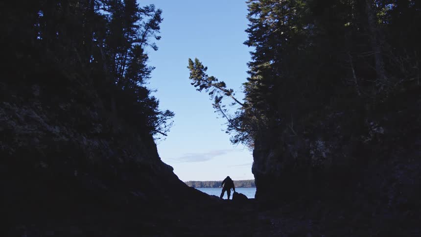 The man climbs down from a rock by the lake