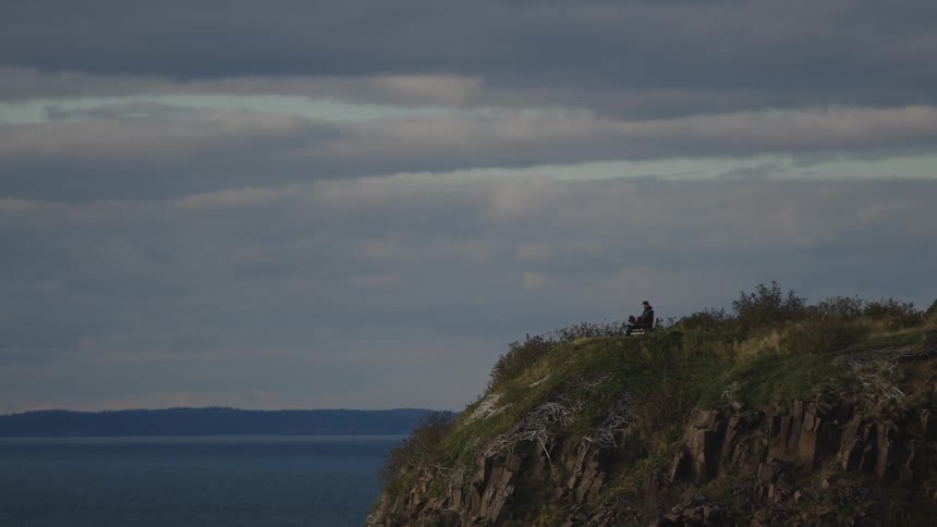 Person sitting alone on a cliff overlooking the sea