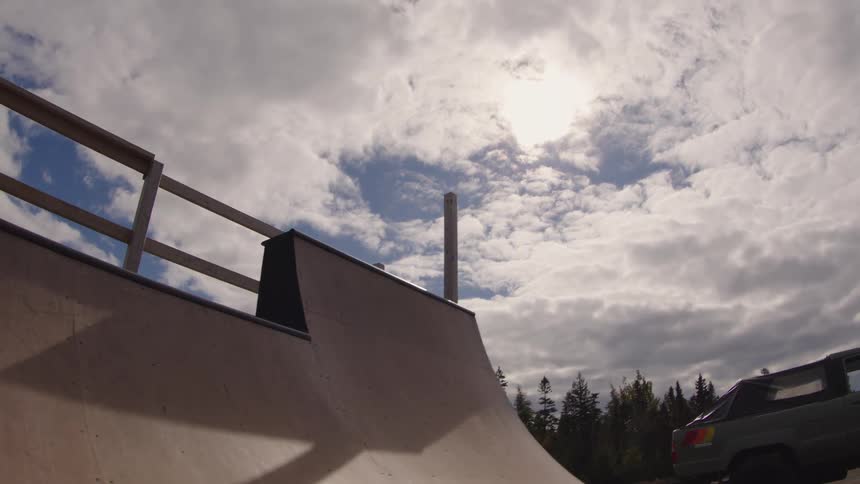 A young man rides his skateboard back and forth on a ramp under the bright sun