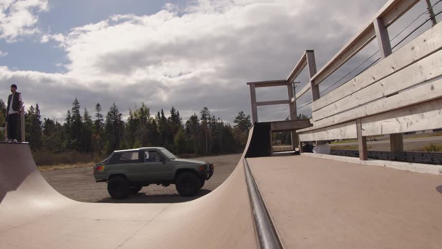 Skateboarder performs a trick on an outdoor ramp under a cloudy sky
