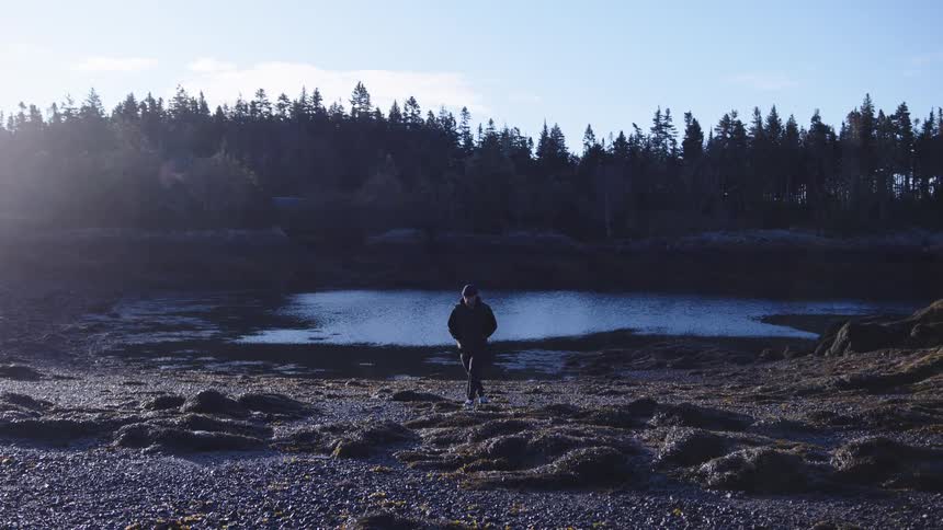 A man in a jacket walks out of a drying lake on a sunny day