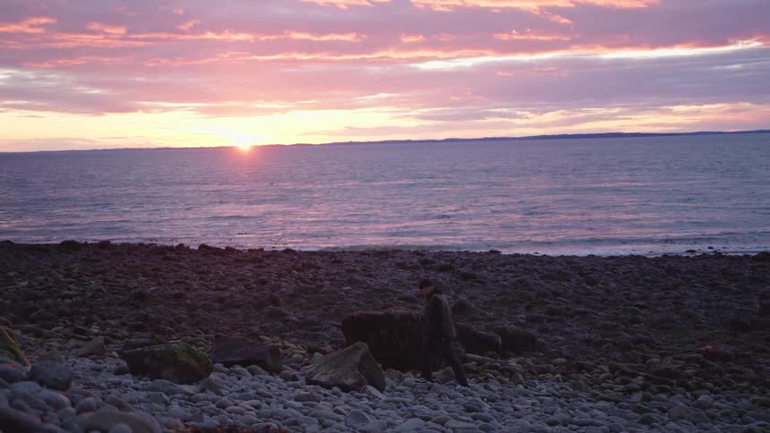 Man walks among rocks by the sea during sunset