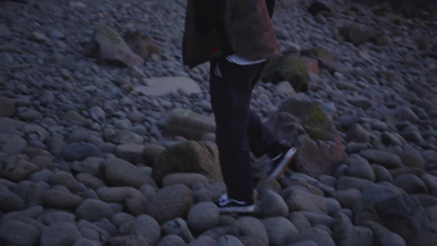 The man walks over the rocks by the shore