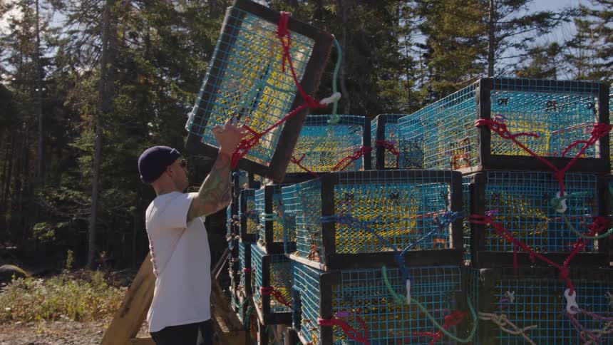 Man stacks blue fishing cages outdoors on a sunny day